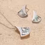Lustrous, iridescent jewellery from the Ormer collection resting on a sandy beach