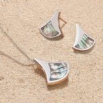 Lustrous, iridescent jewellery from the Ormer collection resting on a sandy beach