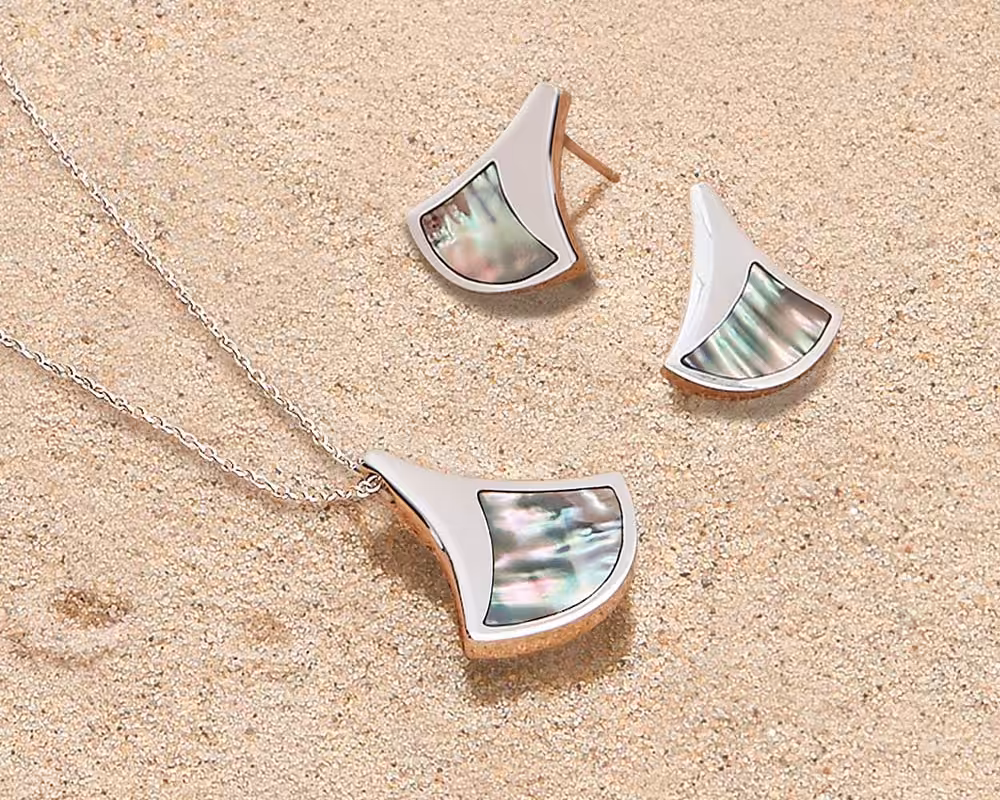 Lustrous, iridescent jewellery from the Ormer collection resting on a sandy beach