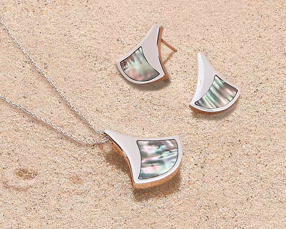 Lustrous, iridescent jewellery from the Ormer collection resting on a sandy beach